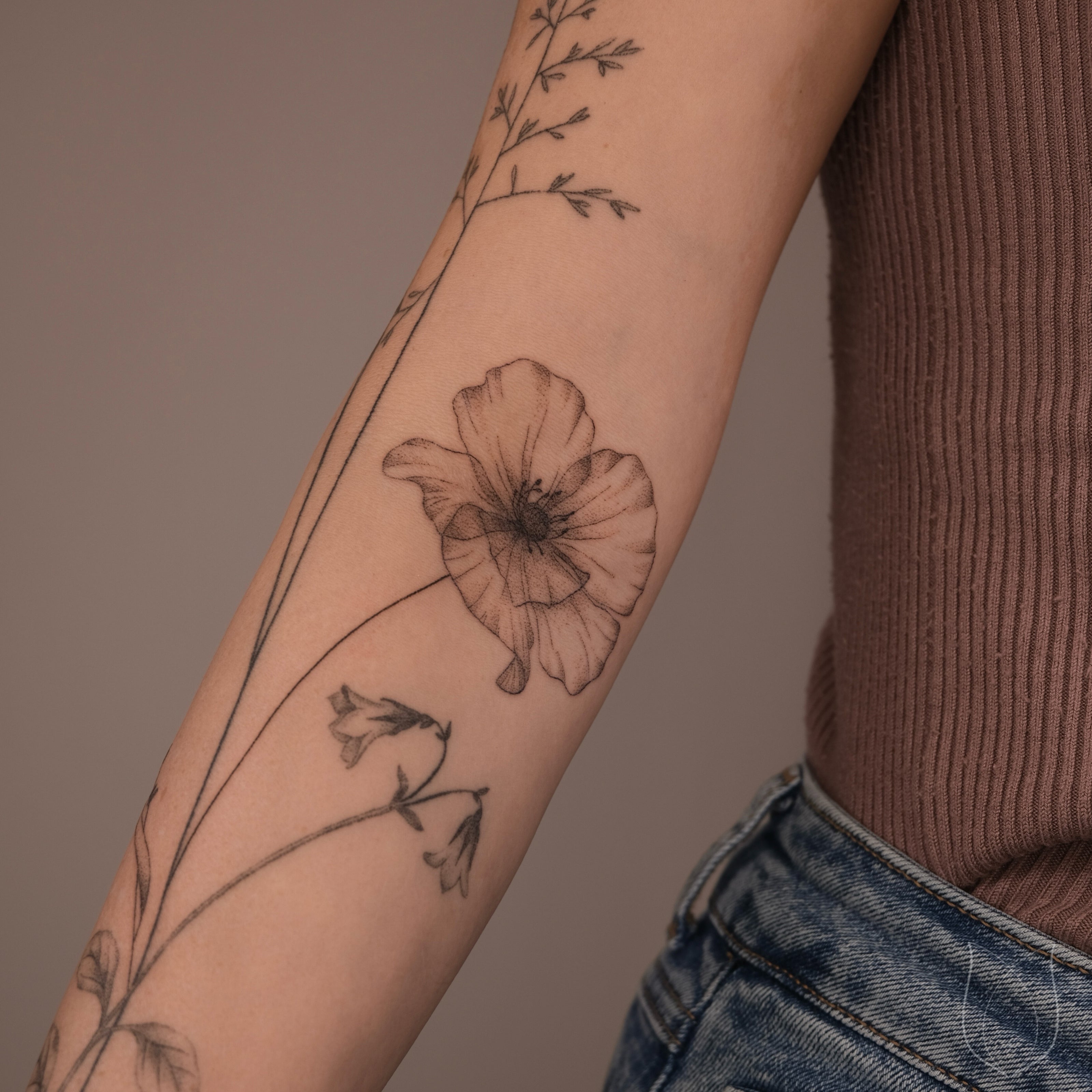 Kleines handgestochenes Mohnblume Tattoo mit filigranen Linien am Unterarm
